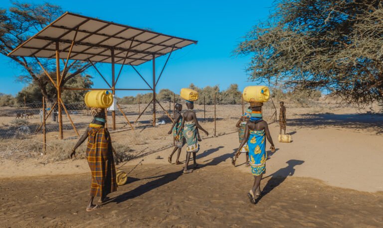 A group of women walk past a solar panel, away from the camera.