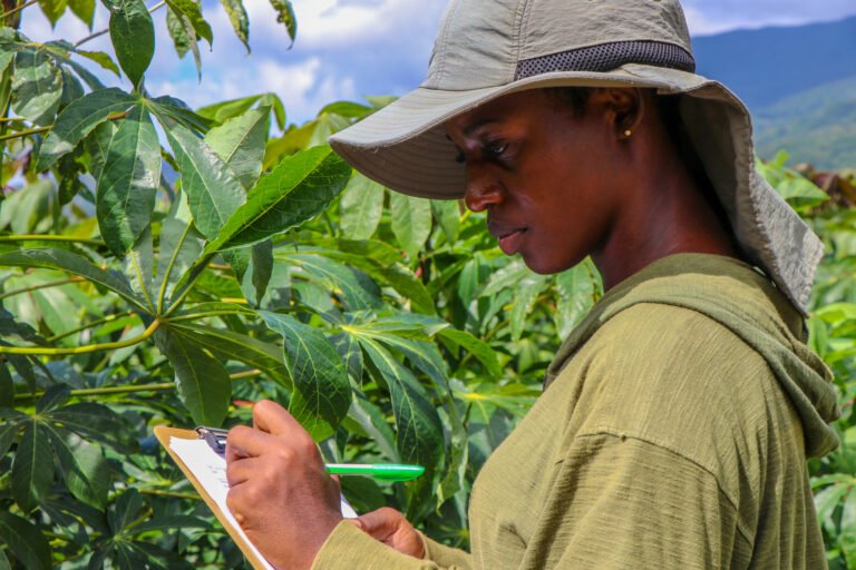 A woman stands in a field, writing on a clipboard.