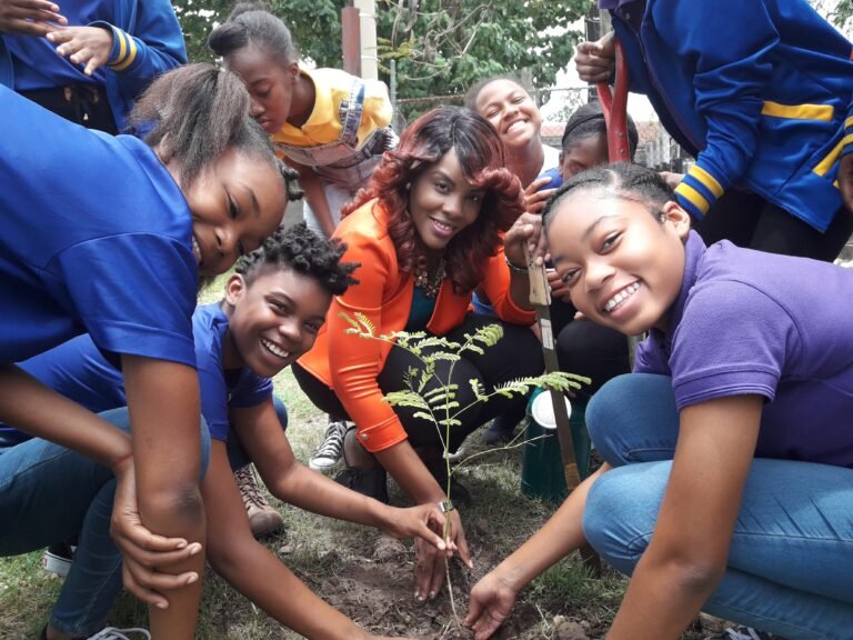 A group of students plants a tree and smiles at the camera.