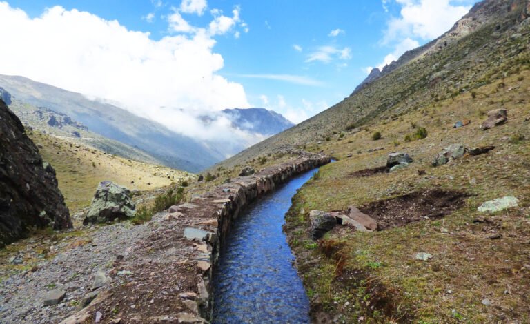 A water canal runs along a mountainside, from the background directly to the camera.