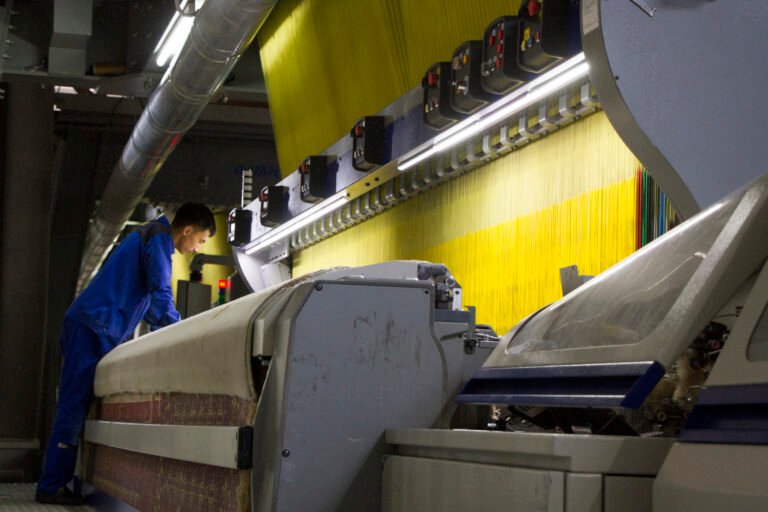 A man stands over a large mechanical loom.