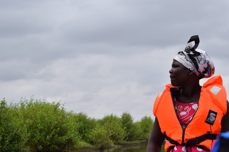 A woman in a bright orange lifejacket looks into the distance.