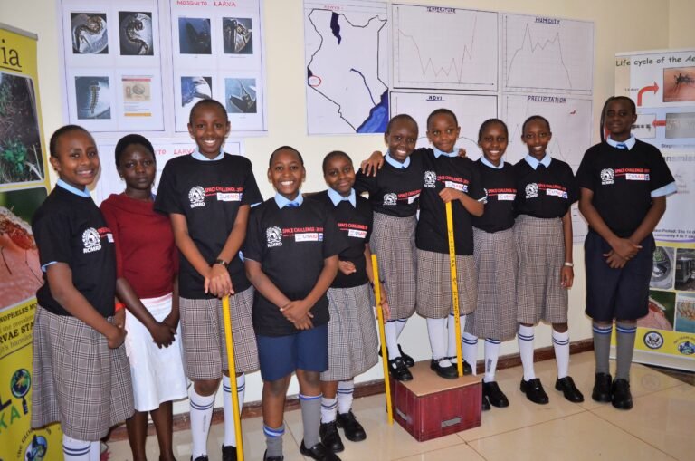A group of students stands in a classroom, facing the camera and smiling.