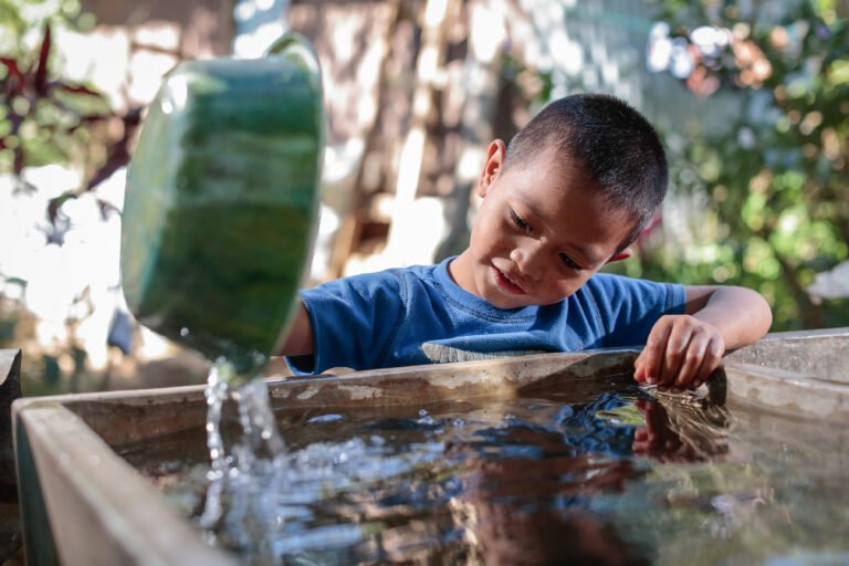 A child pours water from a bowl into a reservoir.