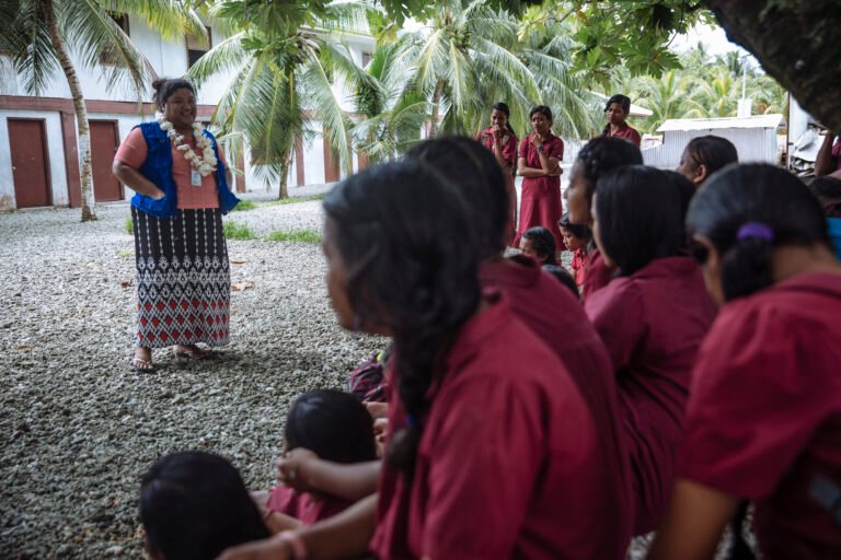 A woman stands in front of a group of other women, leading a discussion.