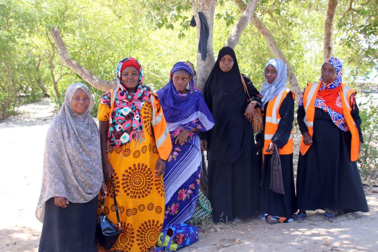 A group of women stands near a coastline, posing for the camera.