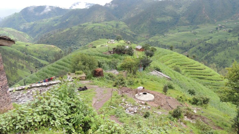Man inspects a rural village water tank surrounded by green hillside.