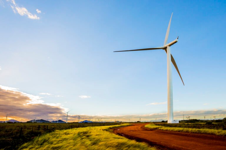 A large wind turbine next to a grass field and dirt road