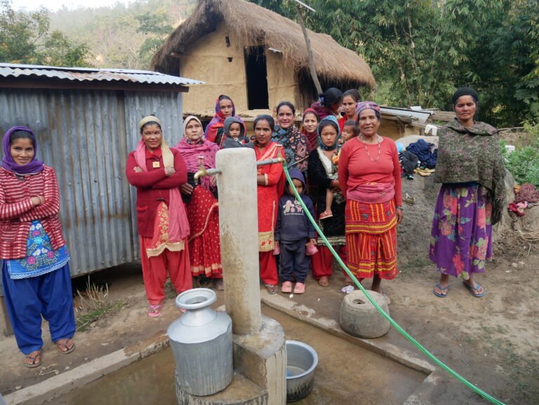 A group of women stands around a Multiple Use Water System (MUS), looking towards the photographer.