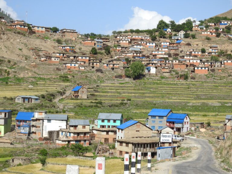 A terraced village sits above and below fields. Many of the houses have blue tin roofs that stand out against the natural tones of the landscape.