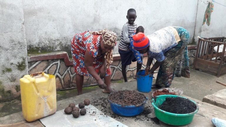 Two women make briquettes while two children sit nearby and watch.