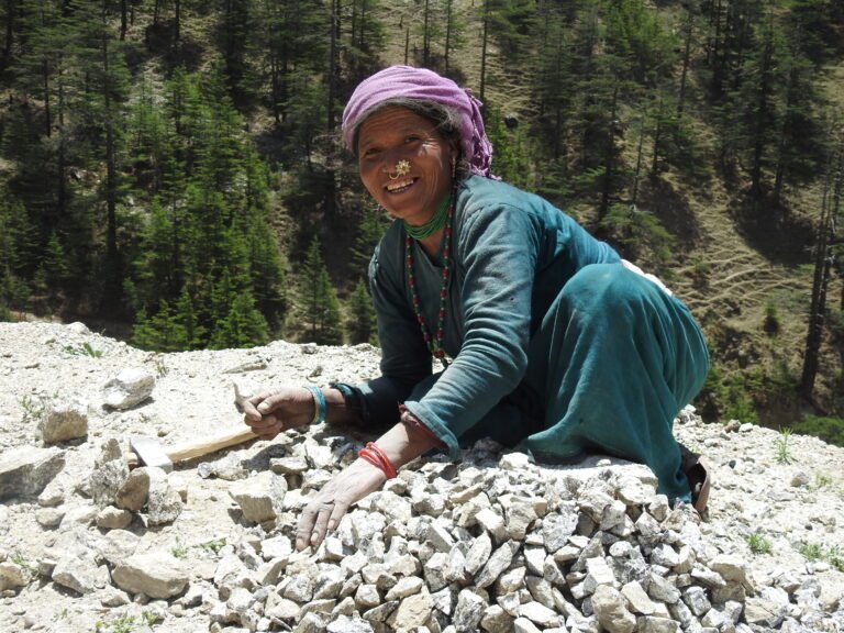 A woman kneels over a pile of stones and smiles at the camera.