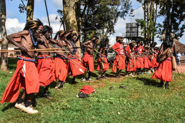 A group of dancers in orange robes stand in a line, jabbing spears in the air.