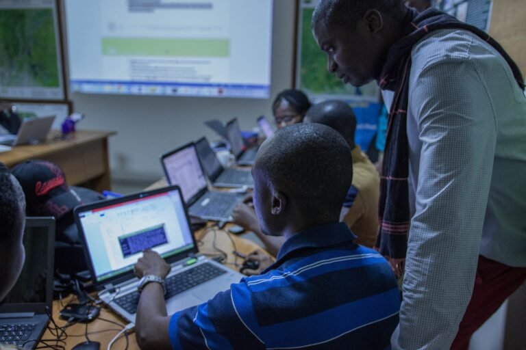 A group of trainees use computers in a classroom while an instructor looks on.