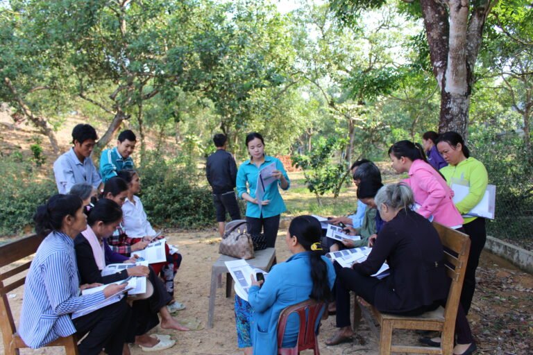 A group of people sit outside and look at documents together.