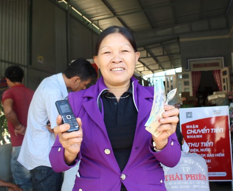 A woman holding a mobile phone in one hand and cash in the other smiles at the camera.