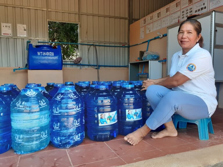 A woman sits next to numerous large plastic water jugs.